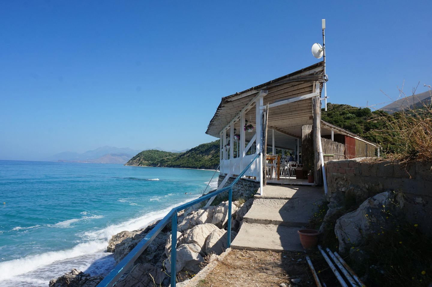Bar rustico in legno sulla spiaggia con vista sul mare turchese e sulle montagne.