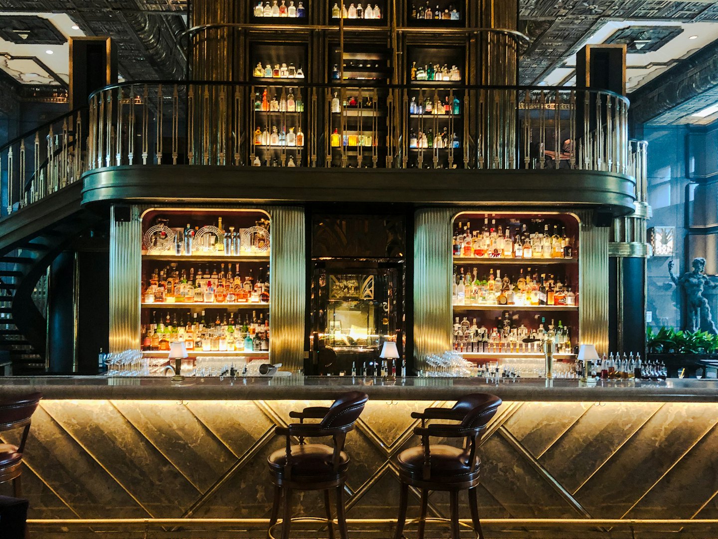 Scaffali illuminati di bottiglie di liquore sopra un bancone bar in marmo.